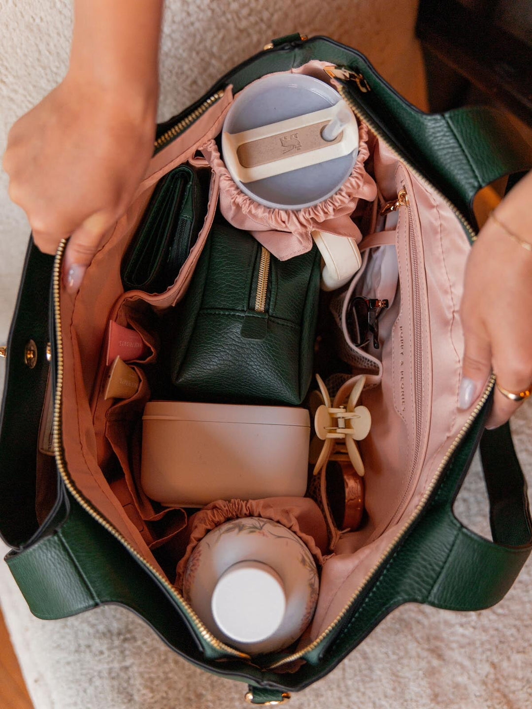 Open handbag revealing various items including a green cosmetic bag and a white lunch box