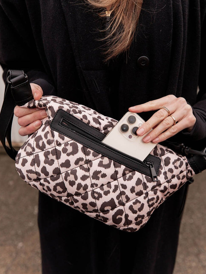 Person holding a leopard print crossbody bag with a phone in it, wearing a black coat.