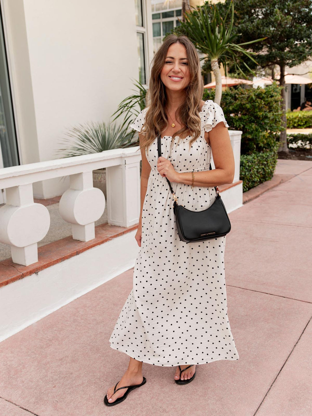 Woman in a polka dot dress wearing a black crossbody bag outdoors
