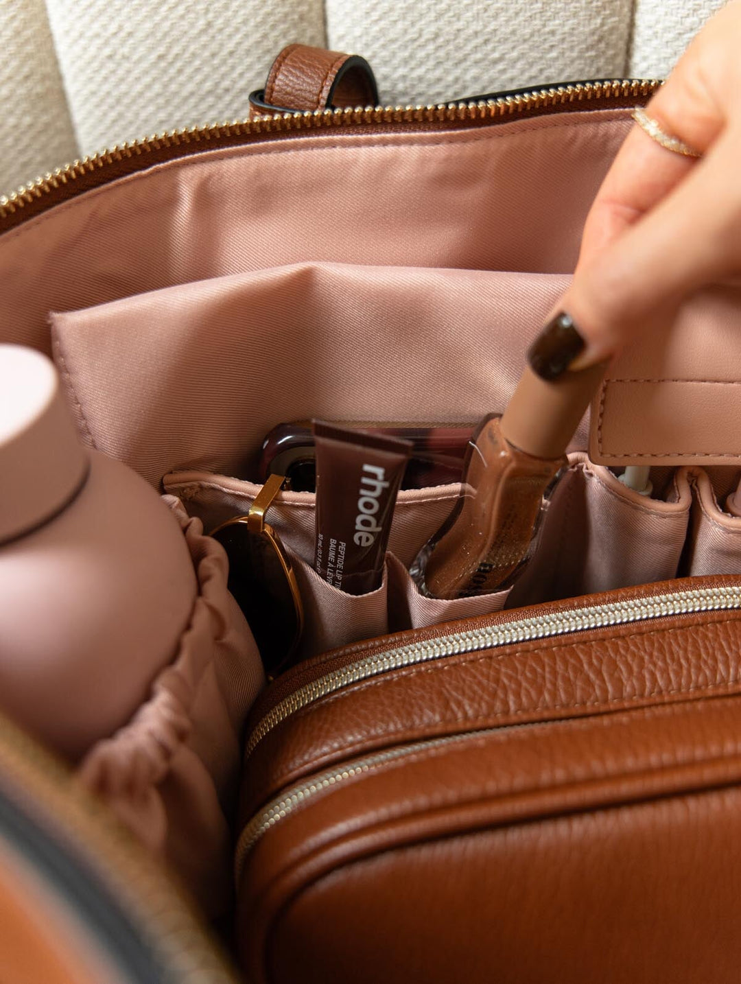 Poppy & Peonies The Knot Tote in Chestnut, featuring blush pink interior pockets holding makeup and everyday essentials, with a hand reaching into the organizer.