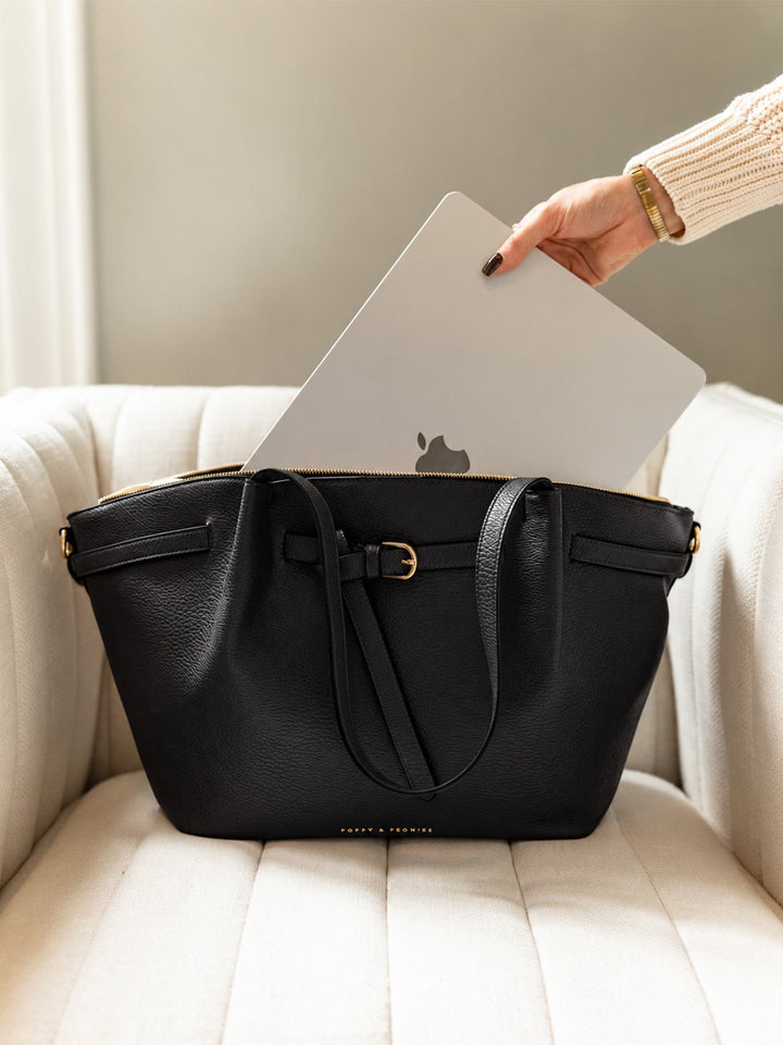 Poppy & Peonies The Knot Tote in Black sitting on a cream chair as a hand places a silver laptop into the bag.