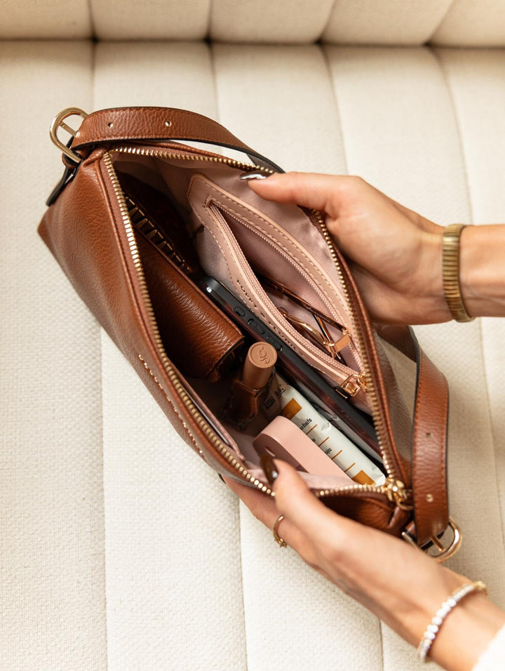 Poppy & Peonies The Soho Shoulder Bag in Chestnut, overhead view of the open zippered compartment filled with everyday essentials, showing the blush-pink lining and interior organization.