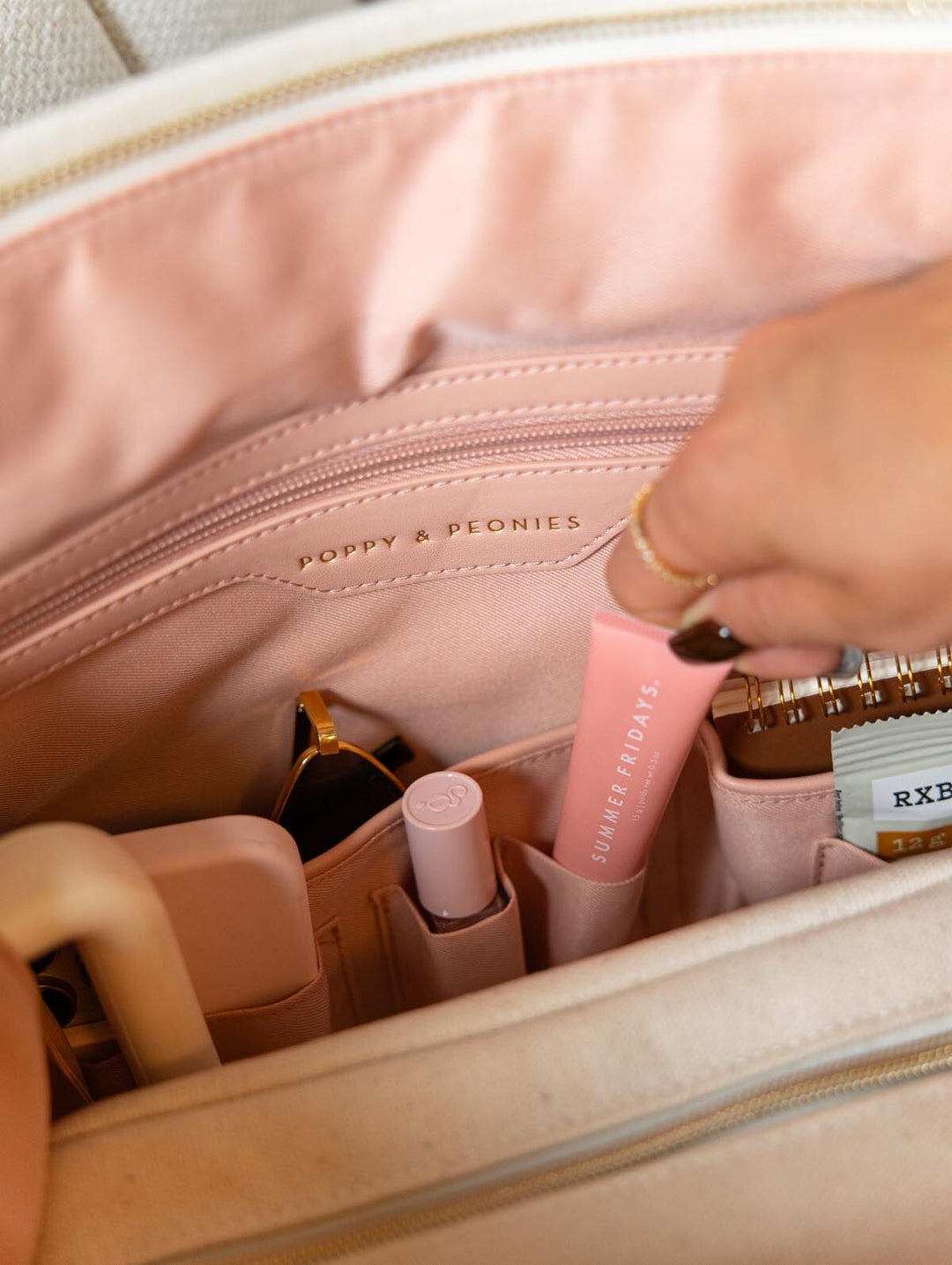Close-up of the interior zippered pocket of Poppy & Peonies The Signature Tote in Olive, with a hand demonstrating the blush pink organizer compartment.