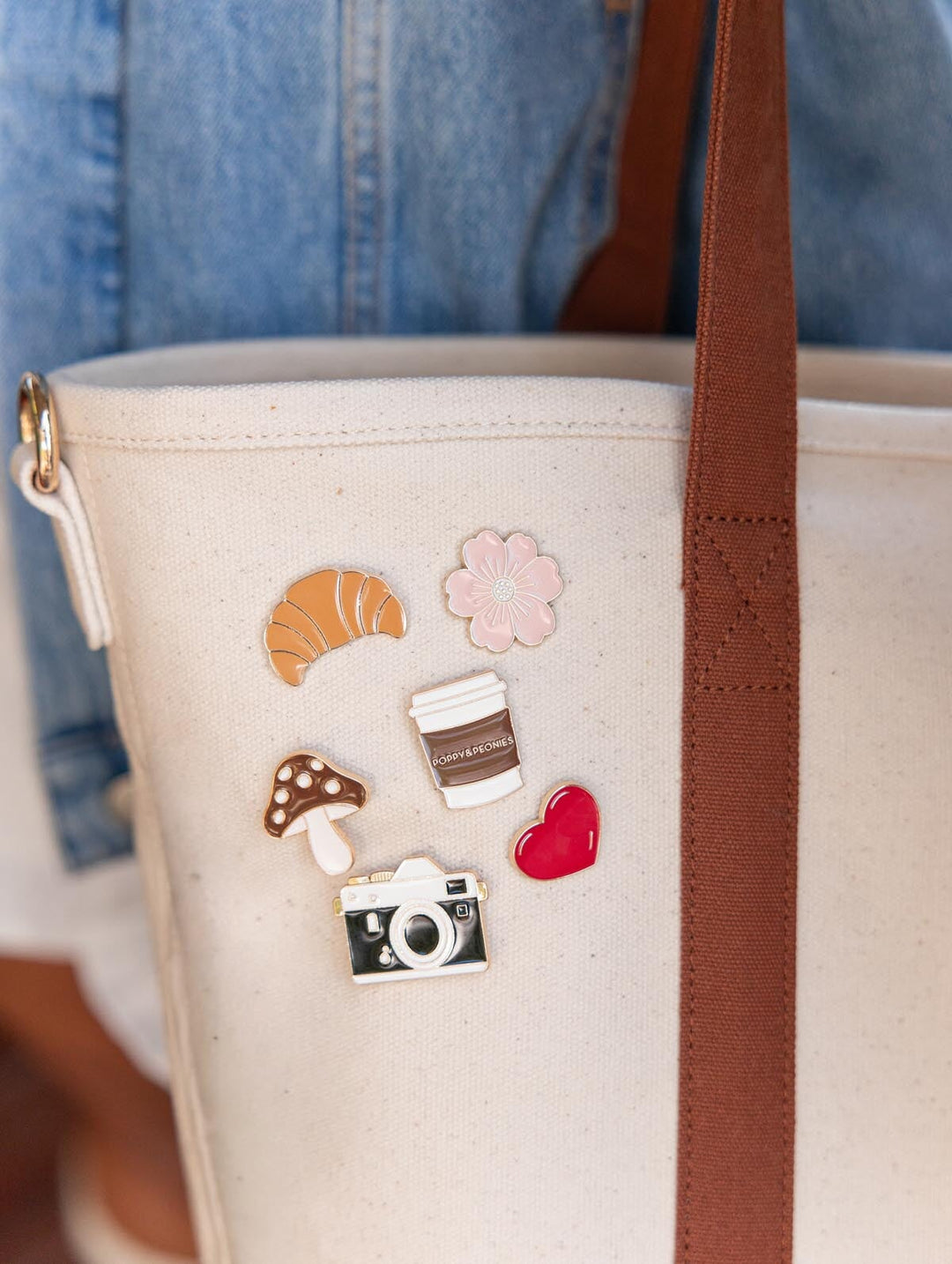 Close-up of Poppy & Peonies The Signature Tote in Chestnut, highlighting decorative pins and patches on the cream canvas beside a chestnut brown handle.