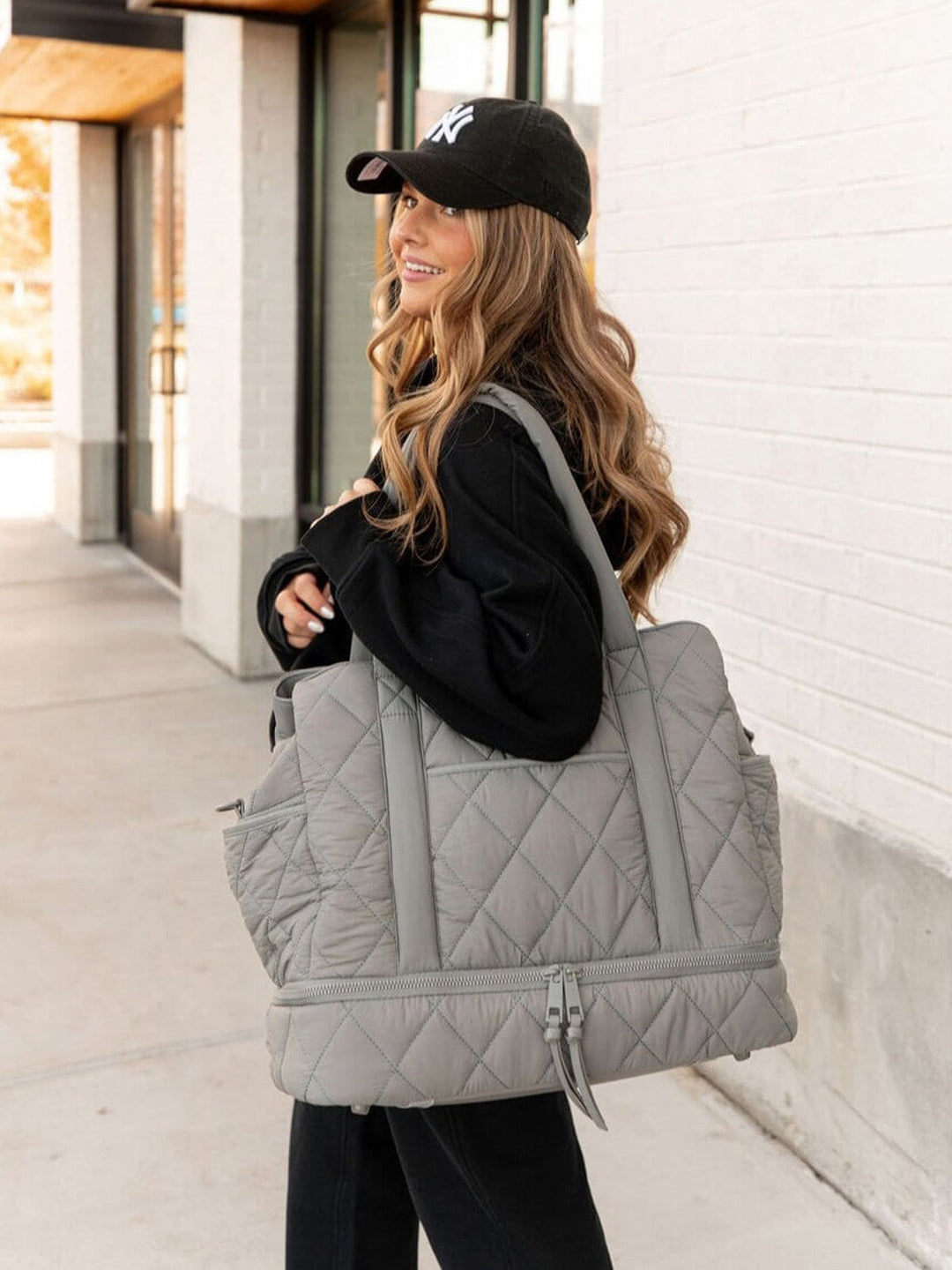 Woman carrying a large grey quilted bag outdoors.