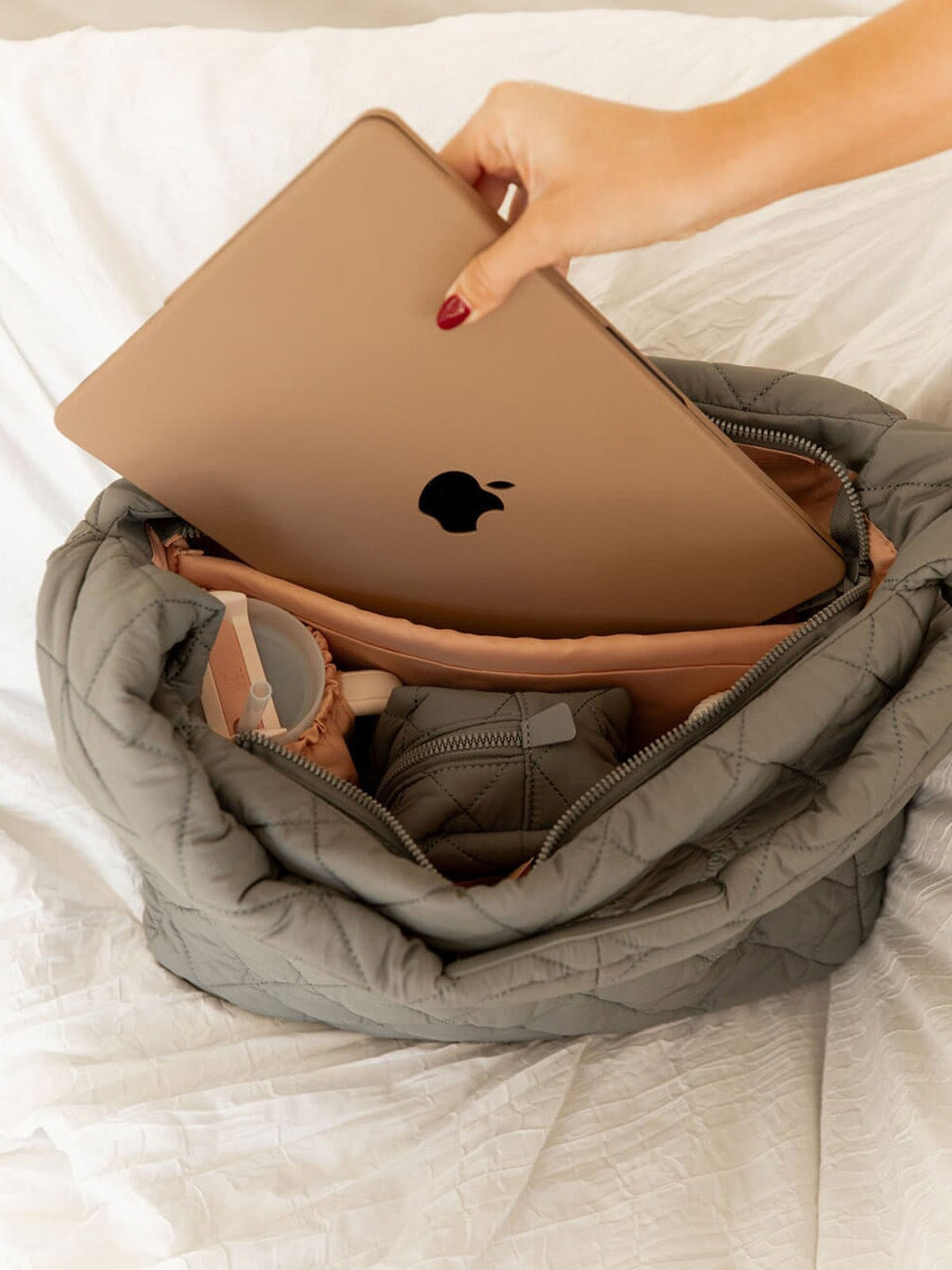 Person placing a laptop into a grey quilted hobo bag on a white surface