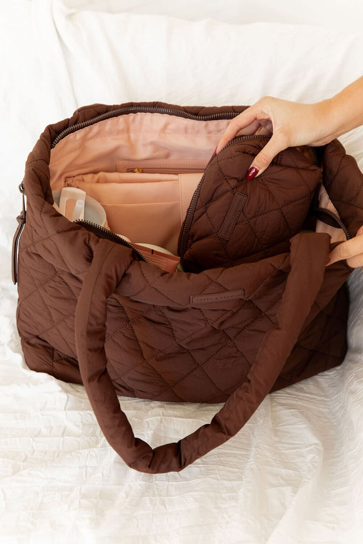 quilted brown cosmetic bag being put into brown quilted hobo bag