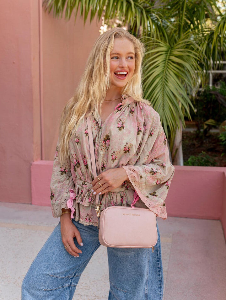 Woman in floral blouse and jeans holding a pink crossbody bag outdoors.