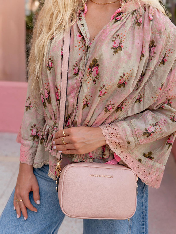 Woman holding a pink crossbody bag wearing a floral blouse and jeans.