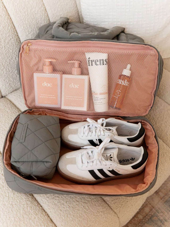 Open travel bag with white sneakers, toiletries, and a grey cosmetic bag.