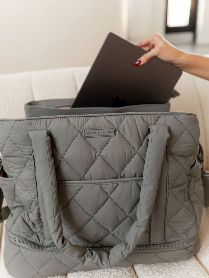 Grey quilted bag with a laptop being placed inside, on a light-coloured couch.