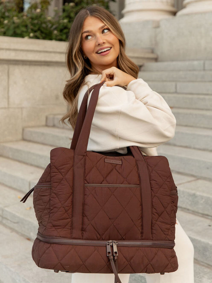 Woman holding a brown quilted bag on stone steps