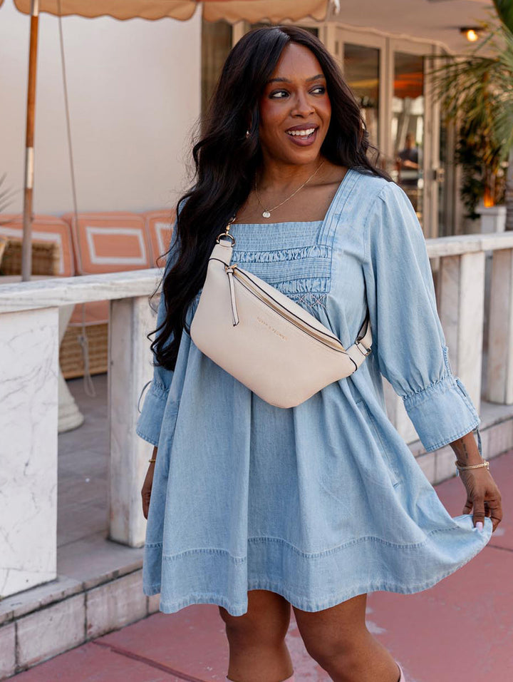 Woman wearing a blue dress and cream crossbody bag