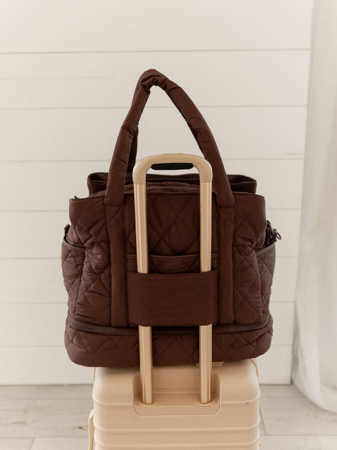 Brown quilted travel bag on a beige suitcase 