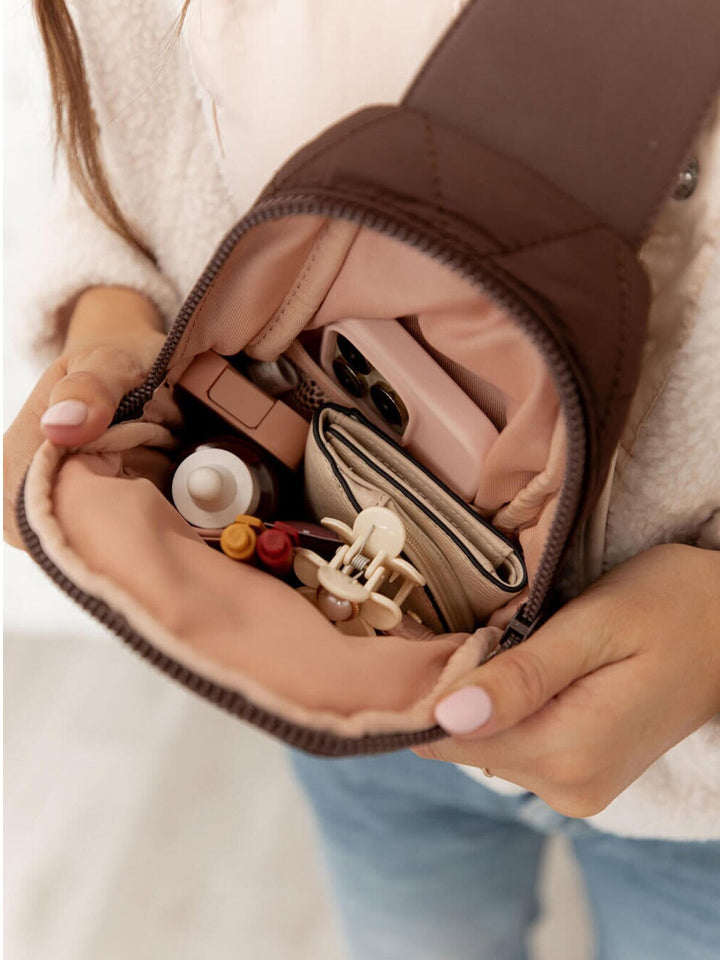 Close-up of a person holding an open brown handbag with various items inside.