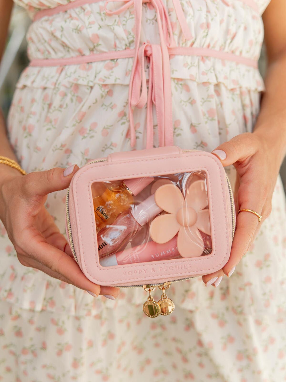 Person holding a pink cosmetic bag with a clear lid, containing beauty products.