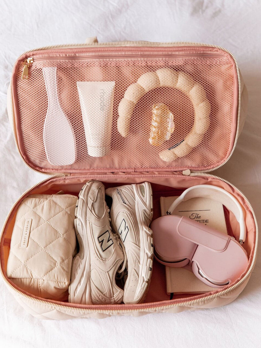Pink travel case with various items including shoes, a brush, and skincare products on a white background