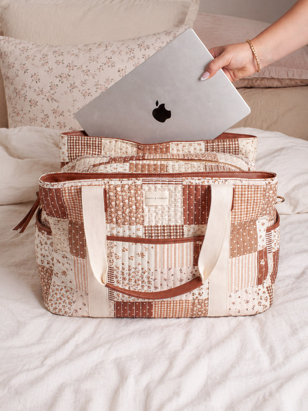 Lifestyle shot of the Mini Voyager in Brown Patchwork, showcasing its spacious zip-top design with a laptop being placed inside for easy everyday or travel organization.